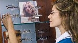A woman in a blue shirt tries on a new pair of glasses